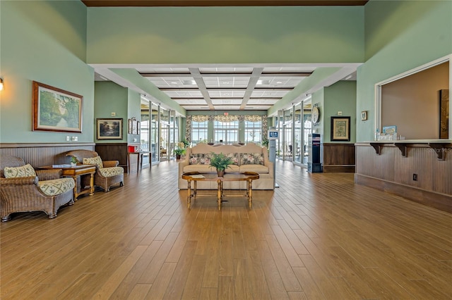 living room featuring beam ceiling, wood walls, coffered ceiling, and light wood-type flooring