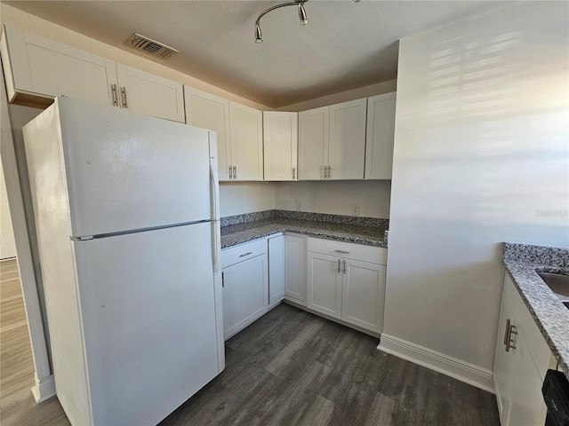 kitchen featuring white cabinets, white fridge, dark stone countertops, and dark wood-type flooring