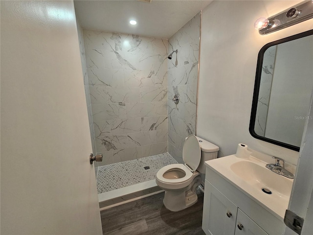 bathroom with tiled shower, hardwood / wood-style floors, vanity, and toilet