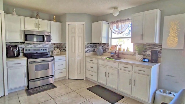 kitchen with sink, stainless steel appliances, light tile patterned floors, backsplash, and white cabinets