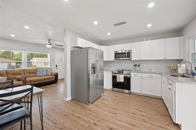 kitchen with light stone countertops, appliances with stainless steel finishes, sink, light hardwood / wood-style flooring, and white cabinetry