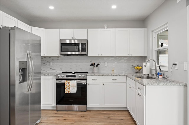 kitchen featuring light stone countertops, sink, light hardwood / wood-style flooring, white cabinets, and appliances with stainless steel finishes