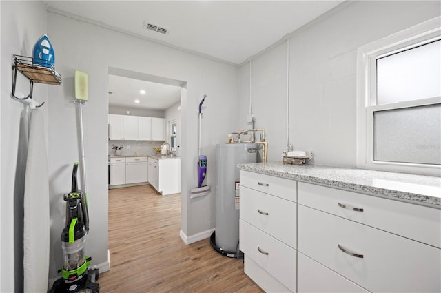 kitchen with white cabinets, sink, water heater, light hardwood / wood-style floors, and light stone counters