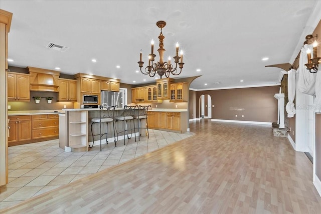 kitchen featuring a kitchen bar, custom exhaust hood, stainless steel appliances, a center island with sink, and a chandelier