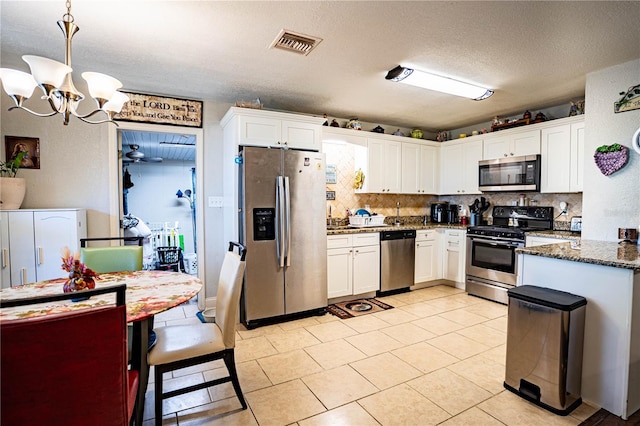 kitchen featuring dark stone countertops, white cabinets, hanging light fixtures, and appliances with stainless steel finishes