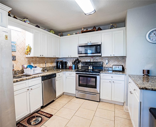 kitchen featuring appliances with stainless steel finishes, tasteful backsplash, white cabinetry, and light stone counters