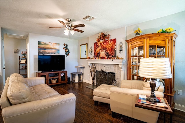 living room featuring a textured ceiling, ceiling fan, dark wood-type flooring, and a tiled fireplace