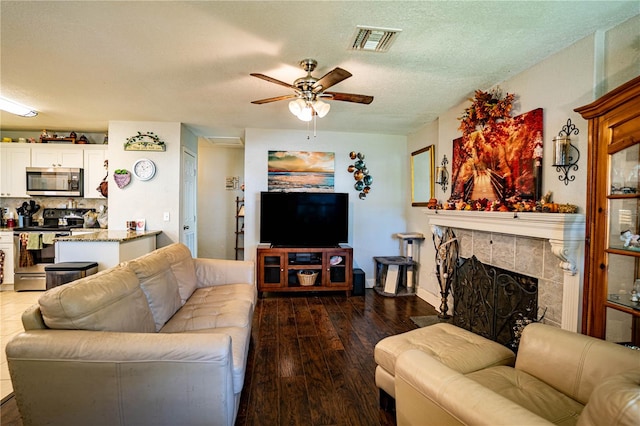 living room with a textured ceiling, ceiling fan, dark hardwood / wood-style flooring, and a fireplace