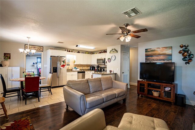 living room with ceiling fan with notable chandelier, a textured ceiling, and light hardwood / wood-style flooring