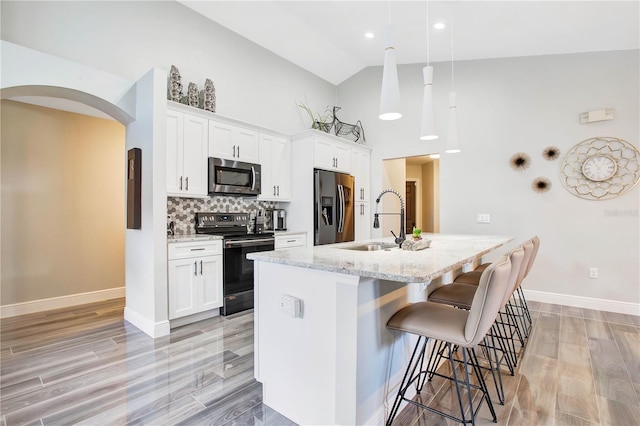 kitchen with white cabinetry, hanging light fixtures, stainless steel appliances, light stone counters, and an island with sink