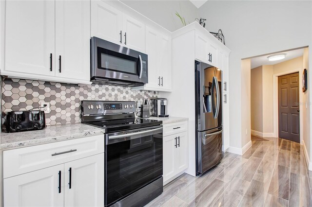 1591 Forest Hills Ln, Haines City, FL 33844 - kitchen featuring appliances with stainless steel finishes, tasteful backsplash, white cabinetry, light stone countertops, and light wood-style flooring