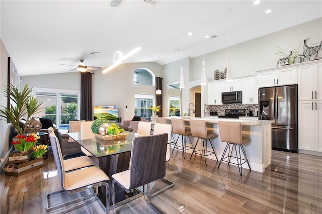 dining space with ceiling fan, high vaulted ceiling, sink, and hardwood / wood-style floors