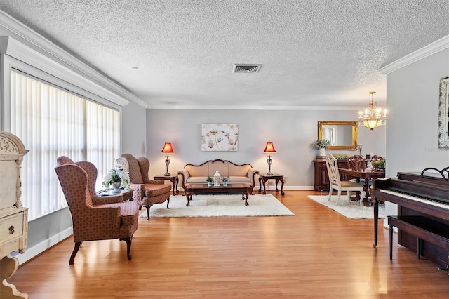 living room with a textured ceiling, a notable chandelier, visible vents, ornamental molding, and light wood-type flooring