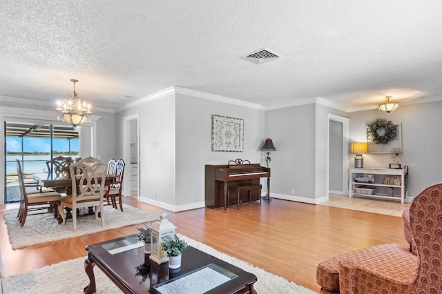 living room featuring ornamental molding, visible vents, a notable chandelier, and wood finished floors