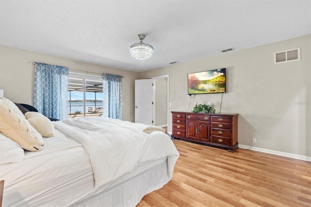 bedroom with a textured ceiling, light wood-type flooring, visible vents, and baseboards