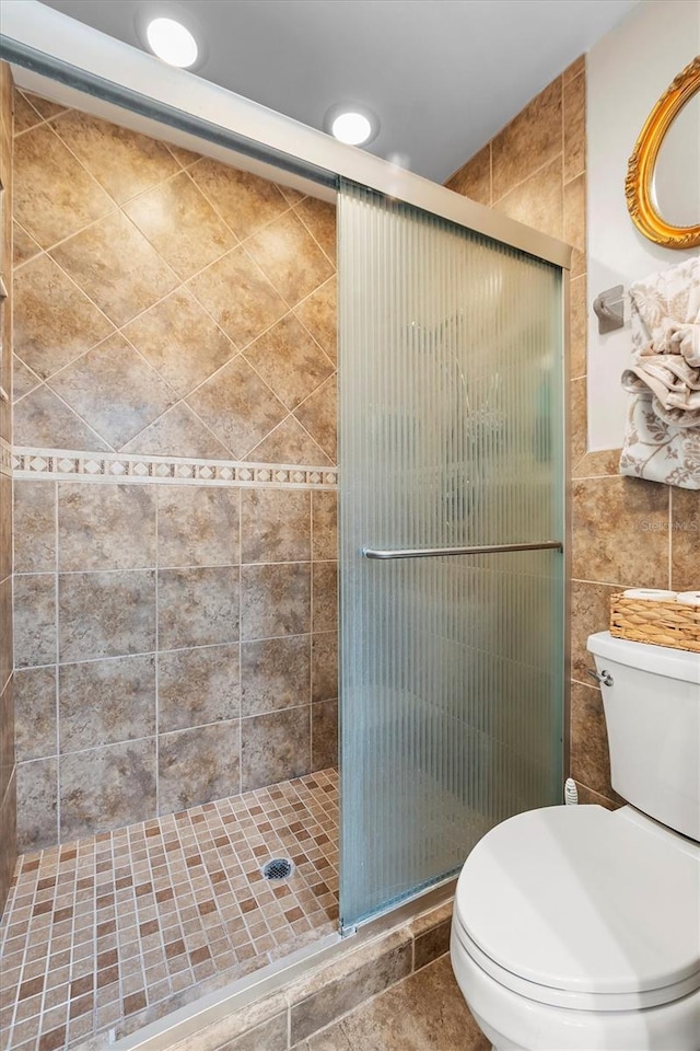 bathroom featuring a shower stall, toilet, and tile walls