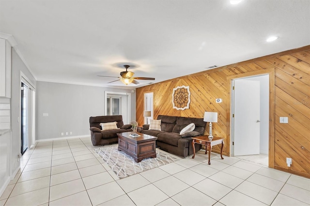 living room featuring light tile patterned floors, ceiling fan, ornamental molding, and wood walls