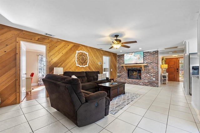 living area featuring visible vents, ceiling fan, wood walls, a brick fireplace, and light tile patterned flooring