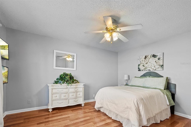 bedroom with light wood-style floors, ceiling fan, baseboards, and a textured ceiling