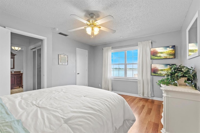 bedroom featuring a textured ceiling, a ceiling fan, baseboards, visible vents, and light wood-style floors