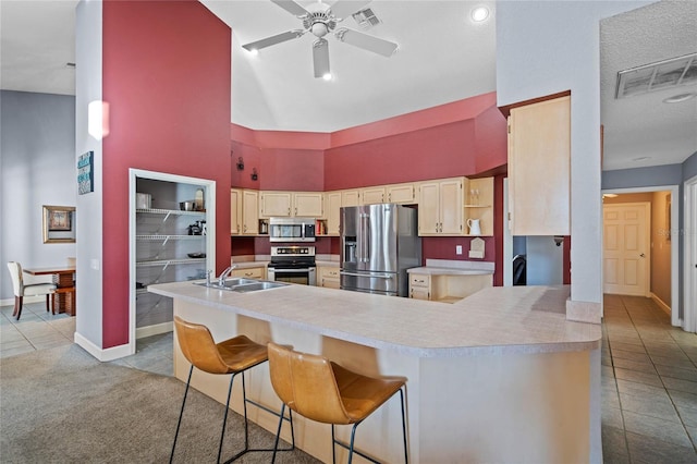 kitchen featuring a breakfast bar, sink, a towering ceiling, appliances with stainless steel finishes, and kitchen peninsula