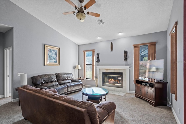 living room with a tile fireplace, vaulted ceiling, ceiling fan, a textured ceiling, and light colored carpet