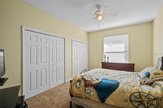 bedroom with carpet flooring, a textured ceiling, two closets, and ceiling fan