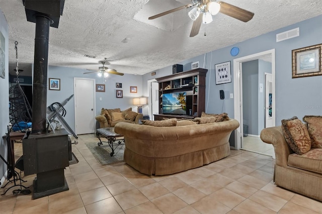 tiled living room featuring a textured ceiling, a wood stove, and ceiling fan