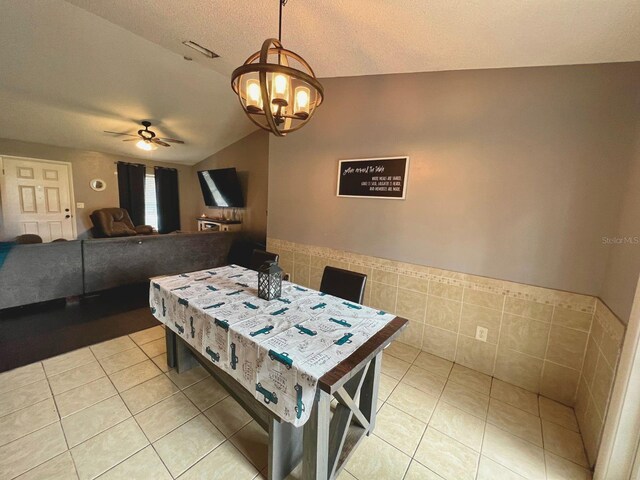 tiled dining space featuring ceiling fan with notable chandelier, tile walls, a textured ceiling, and vaulted ceiling