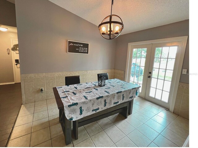 tiled dining space with french doors, a textured ceiling, an inviting chandelier, and tile walls