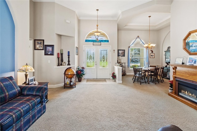 carpeted entrance foyer with french doors, a towering ceiling, ornamental molding, and a chandelier