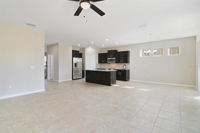 kitchen with backsplash, ceiling fan with notable chandelier, stainless steel appliances, pendant lighting, and a center island with sink