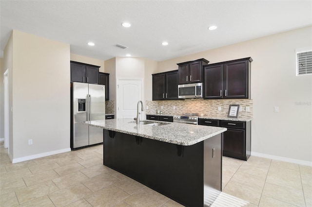 kitchen featuring sink, light stone counters, an island with sink, a breakfast bar, and appliances with stainless steel finishes