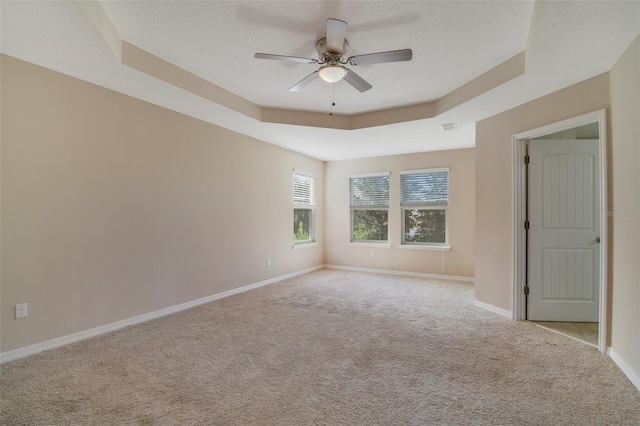 spare room with a tray ceiling, ceiling fan, and light colored carpet