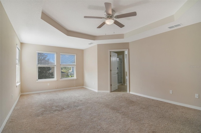 carpeted spare room featuring a tray ceiling and ceiling fan