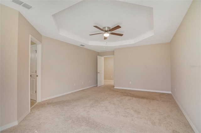 unfurnished room with a tray ceiling, ceiling fan, and light colored carpet