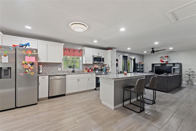 kitchen with a center island, light hardwood / wood-style flooring, appliances with stainless steel finishes, light stone counters, and white cabinetry