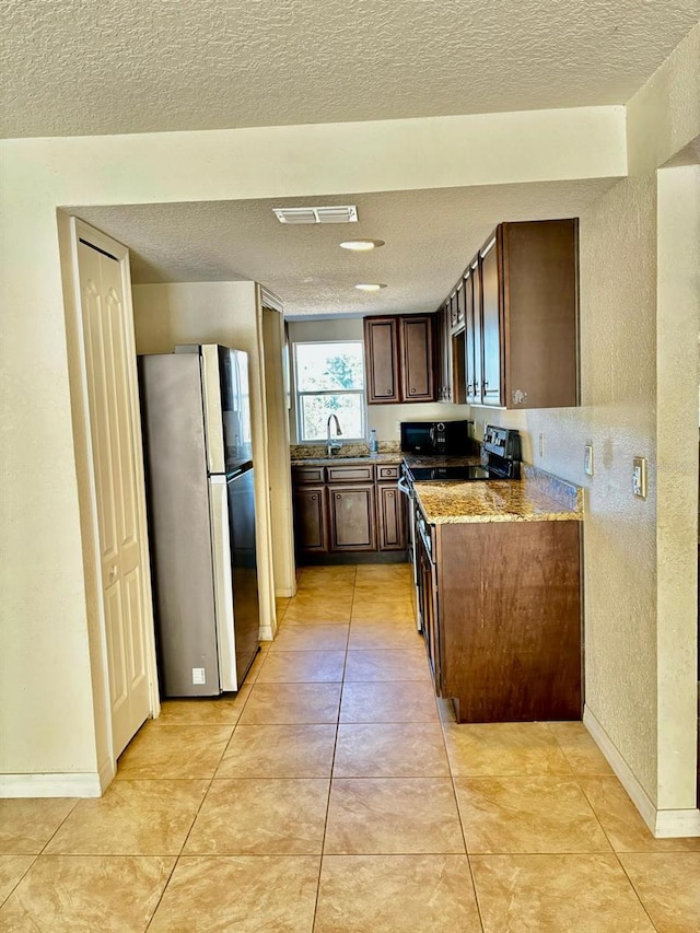 kitchen with black appliances, sink, a textured ceiling, light tile patterned flooring, and light stone counters