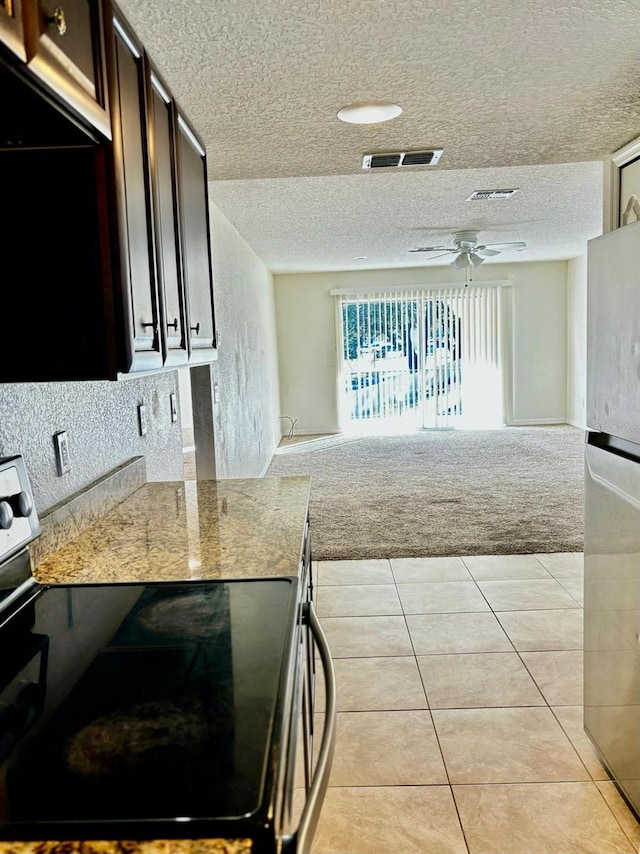 kitchen featuring appliances with stainless steel finishes, a textured ceiling, light colored carpet, and dark brown cabinets