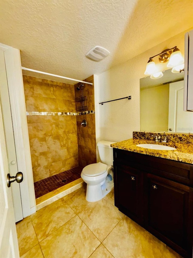 bathroom with tile patterned floors, a textured ceiling, tiled shower, toilet, and vanity