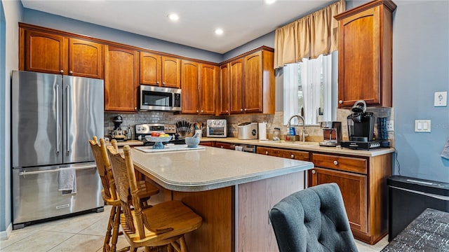 kitchen with a breakfast bar, sink, light tile patterned floors, stainless steel appliances, and backsplash