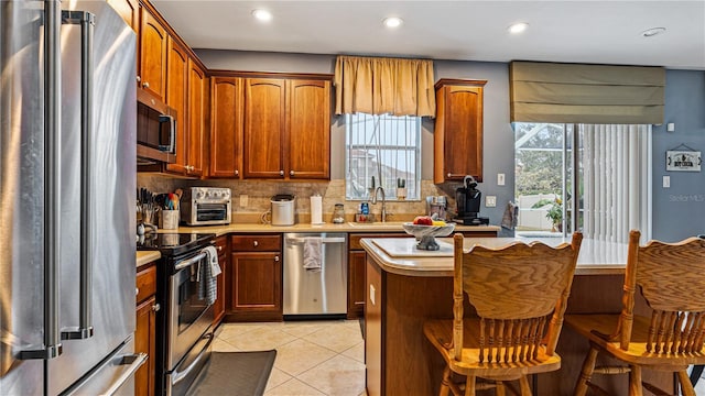 kitchen featuring light tile patterned flooring, appliances with stainless steel finishes, sink, a kitchen breakfast bar, and decorative backsplash