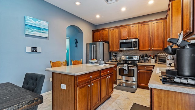 kitchen with light tile patterned flooring, appliances with stainless steel finishes, a center island, and backsplash