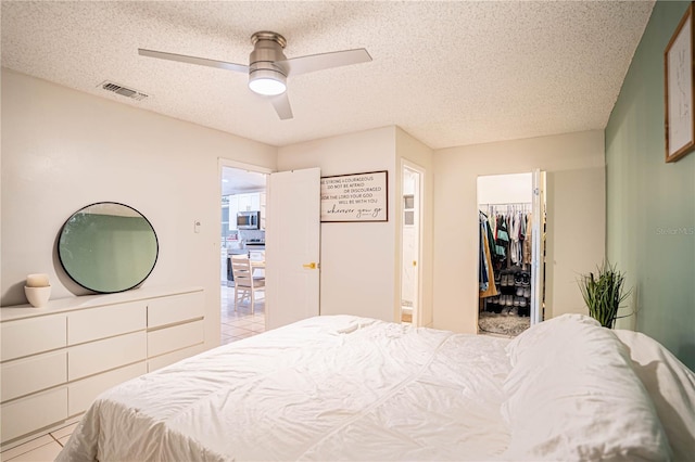 tiled bedroom with a textured ceiling, a spacious closet, a closet, and ceiling fan