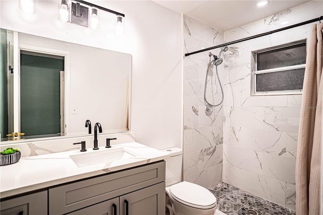 bathroom with tiled shower, vanity, and toilet