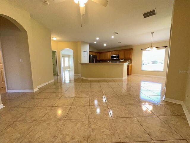 kitchen featuring kitchen peninsula, appliances with stainless steel finishes, ceiling fan with notable chandelier, light tile patterned floors, and pendant lighting