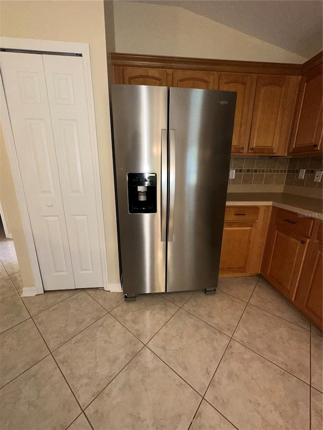 kitchen with vaulted ceiling, stainless steel fridge with ice dispenser, light tile patterned floors, and tasteful backsplash