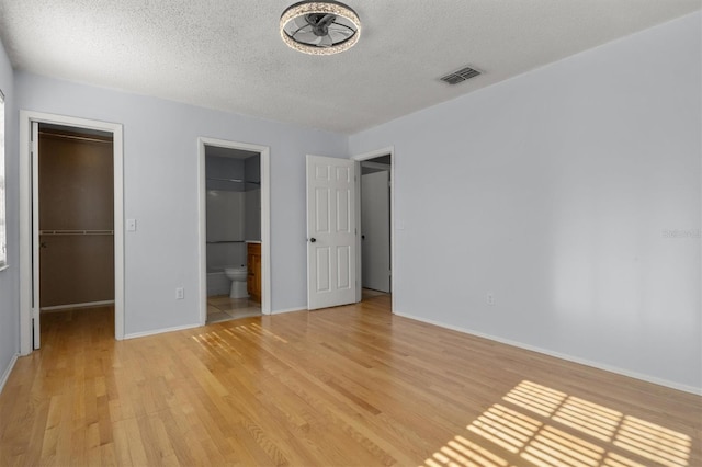 unfurnished bedroom with light hardwood / wood-style floors, a spacious closet, connected bathroom, and a closet