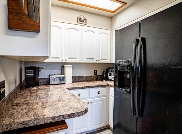 kitchen with a skylight, black fridge, and white cabinets