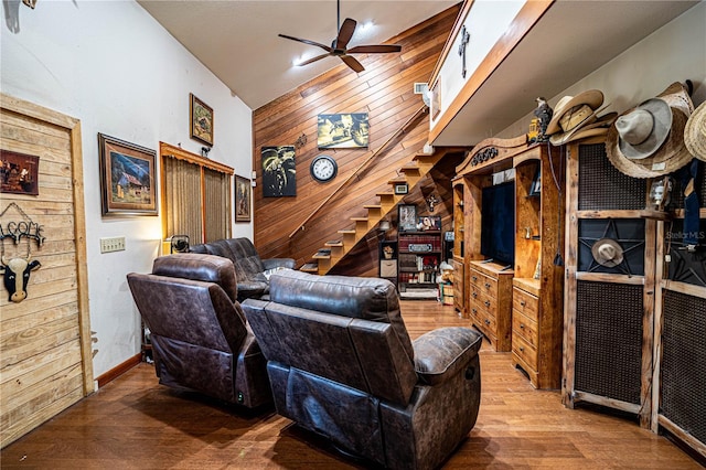 living room featuring ceiling fan, wood walls, wood-type flooring, and high vaulted ceiling